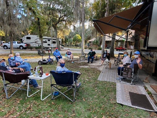 People sitting in camp chairs outside motorhomes.